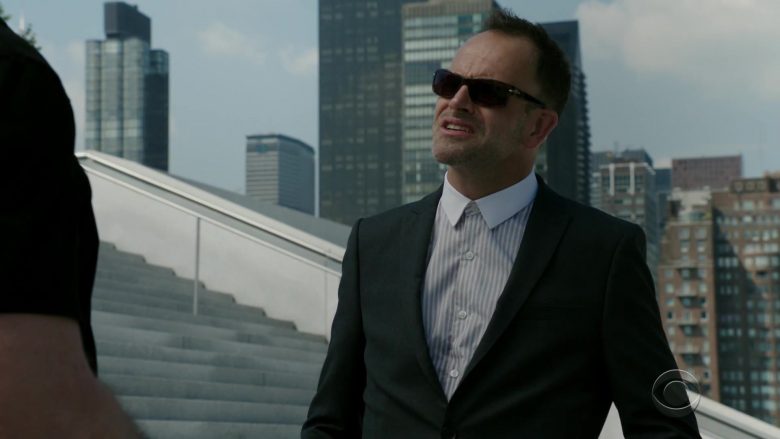 A man wearing a suit and sunglasses standing outside of a building