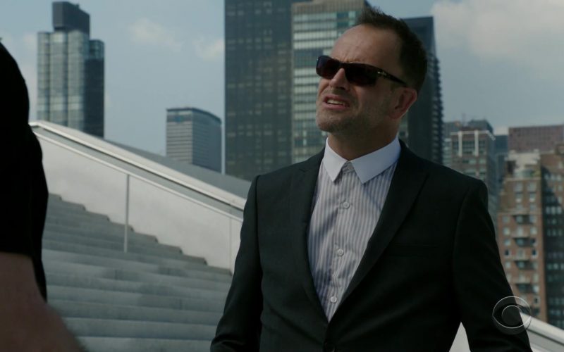 A man wearing a suit and sunglasses standing outside of a building